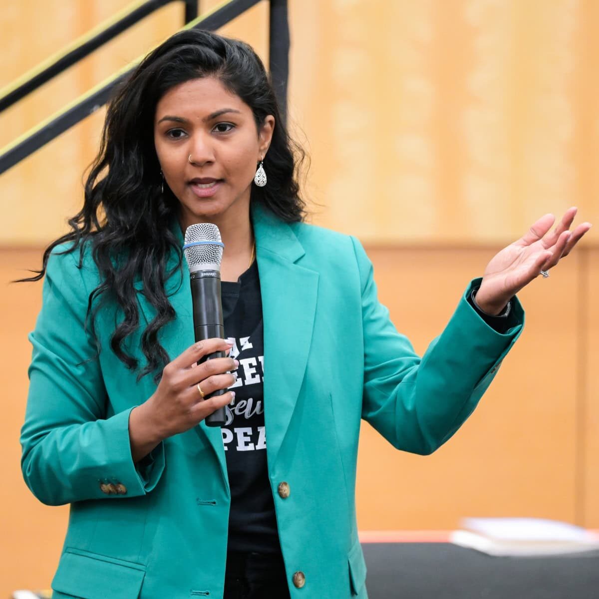 Education-Center A woman in a green jacket holding a microphone and speaking at a conference