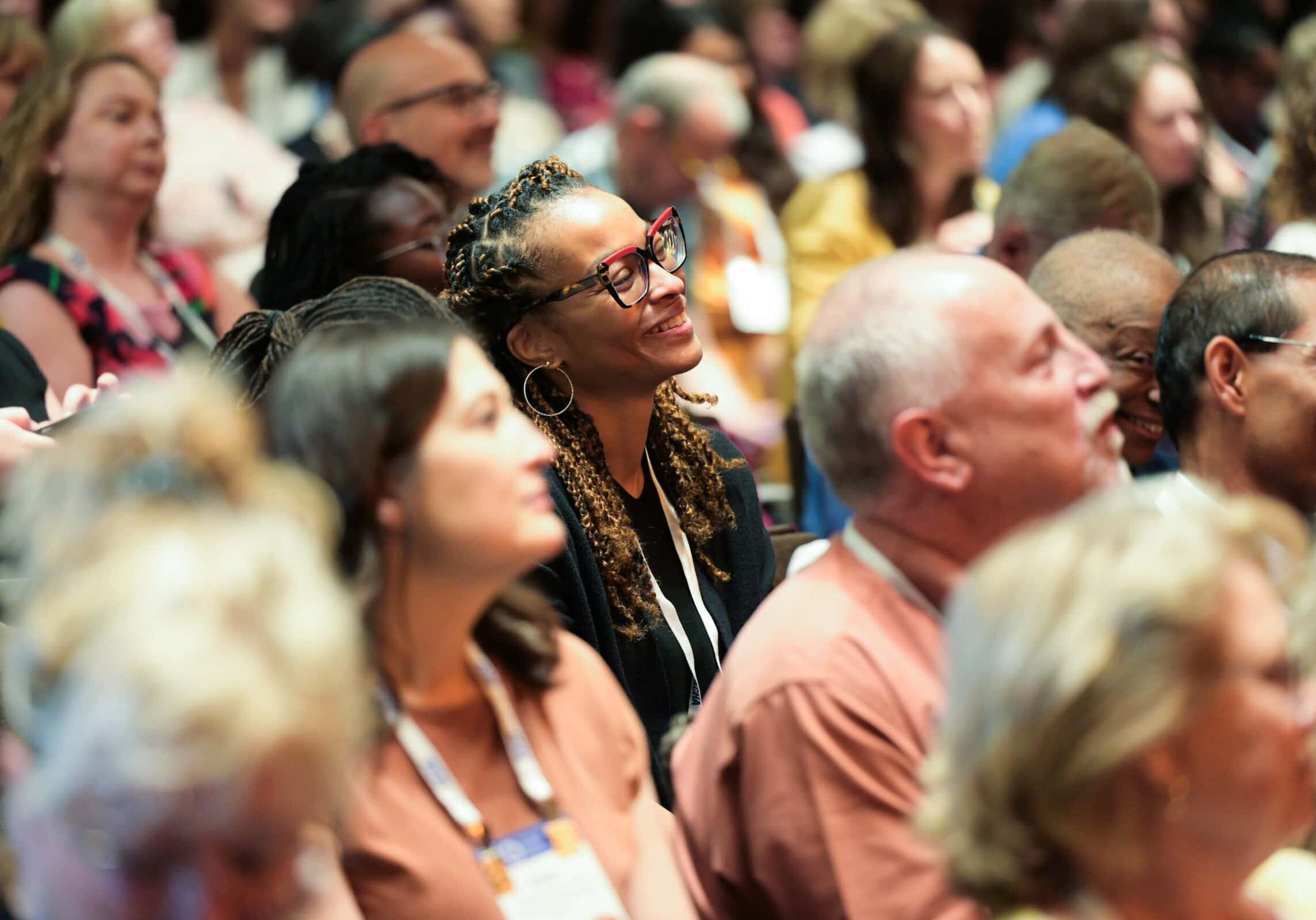 Upcoming ACHA Events Smiling woman sitting in an audience of conference attendees.